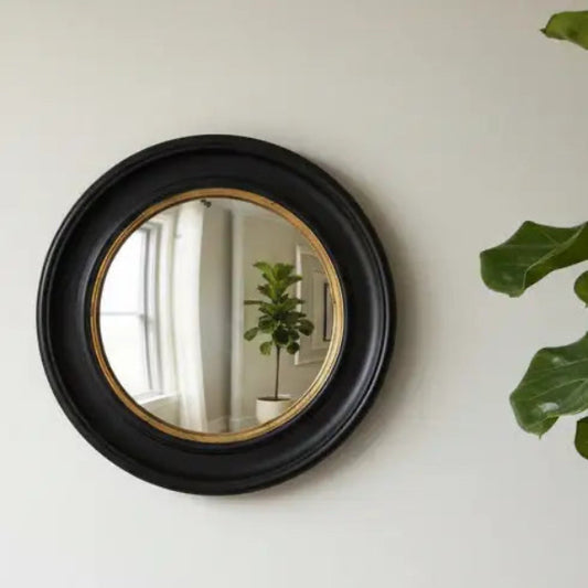 Round black-framed mirror on a wall with decorative items around it.