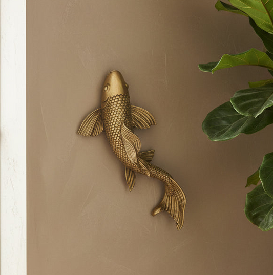 Gold fish wall decoration on a beige wall with a plant in the corner