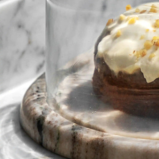 Pastry with white icing and yellow sprinkles under a glass dome on a marble surface