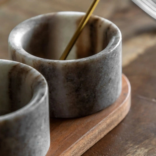 Two stone cups on a wooden surface with a spoon inside one of them.