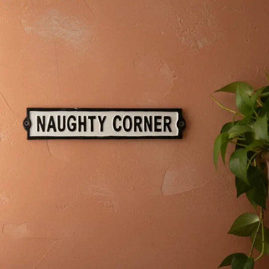 Sign with 'NAUGHTY CORNER' text on a textured wall with a plant.