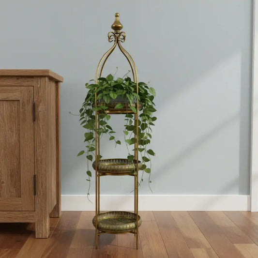 Decorative gold plant stand with green plants against a light gray wall.