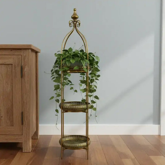 Decorative gold plant stand with green plants against a light gray wall.