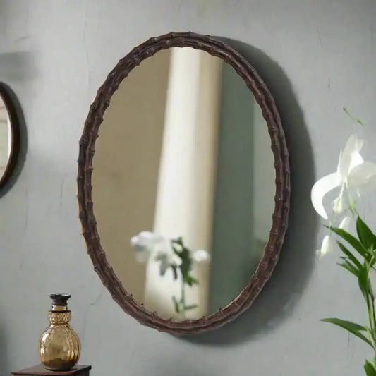 Oval mirror with a decorative brown frame on a white background