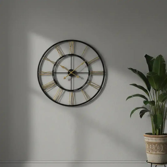 Large wall clock with gold accents on a gray wall next to a potted plant.