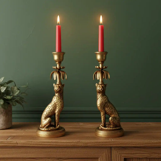 Two gold cheetah-shaped candle holders with red candles on a wooden surface against a green wall.