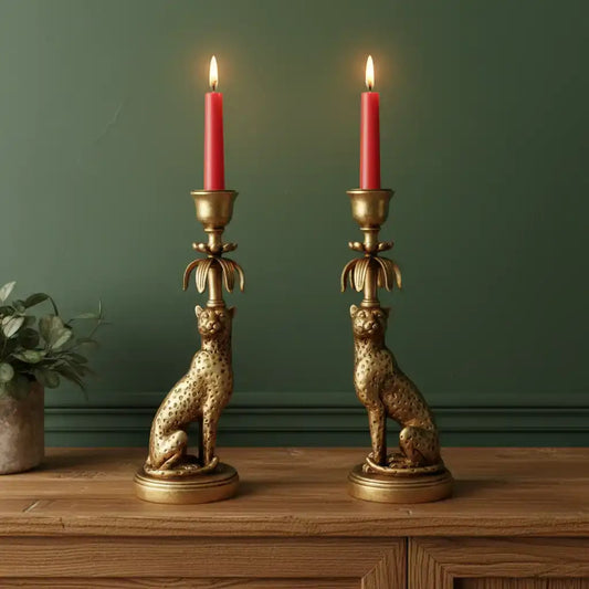 Two gold cheetah-shaped candle holders with red candles on a wooden surface against a green wall.
