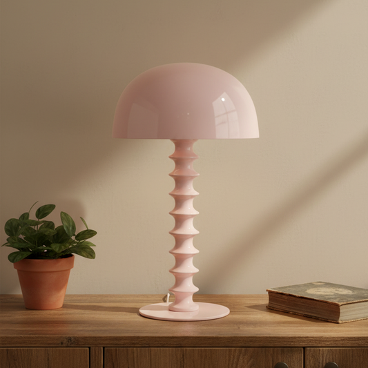 Pink table lamp on a wooden surface with a plant and book in the background