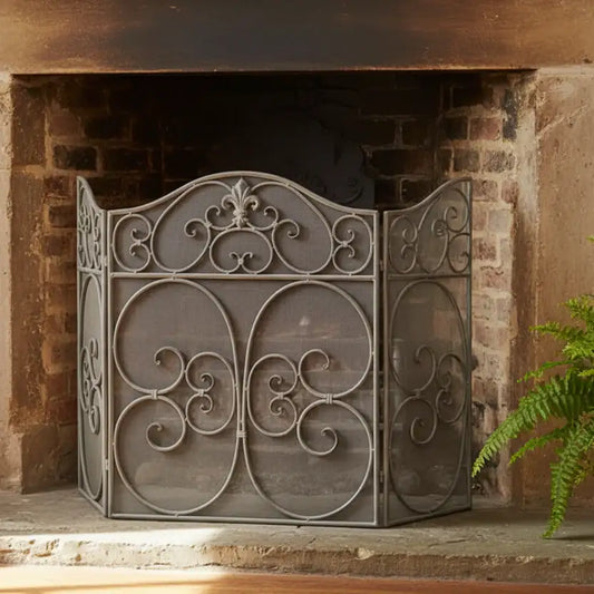 Decorative metal fireplace screen in front of a brick fireplace with a plant to the right.