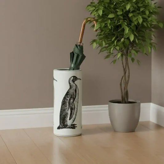 Umbrella stand with penguin design holding an umbrella next to a potted plant on a wooden floor.