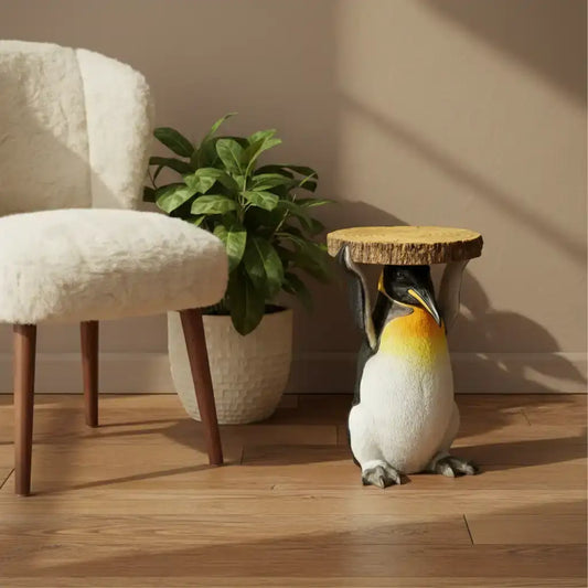 Penguin statue next to a chair and plant on a wooden floor.
