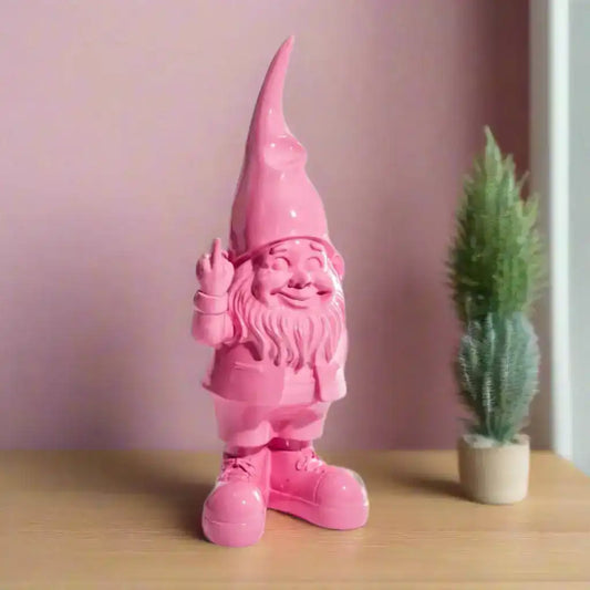 Pink gnome figurine waving next to a small potted plant on a wooden surface with a light purple wall background.