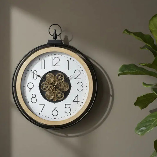 Decorative wall clock with gear detail on a beige wall, next to a plant.