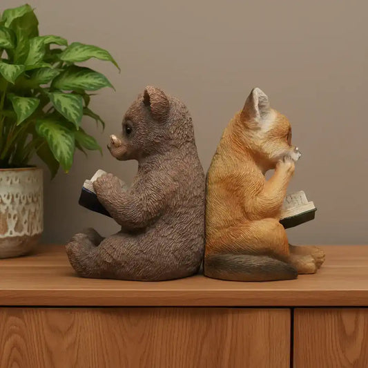 Two animal figurines, one resembling a bear and the other a fox, sitting on a wooden surface with books.