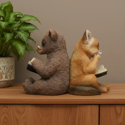 Two animal figurines, one resembling a bear and the other a fox, sitting on a wooden surface with books.