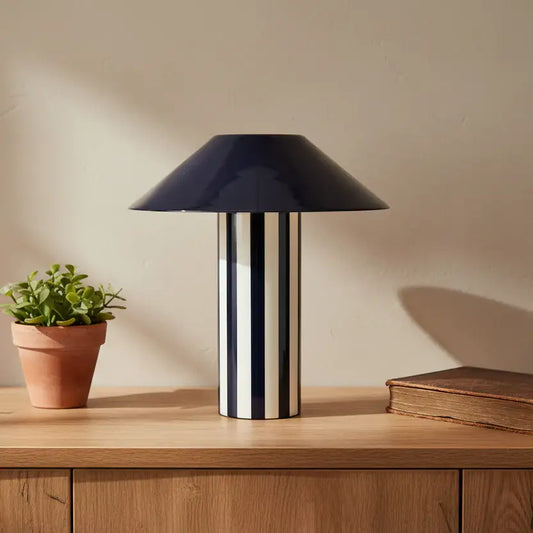 Black table lamp on a wooden surface with a plant and book in the background
