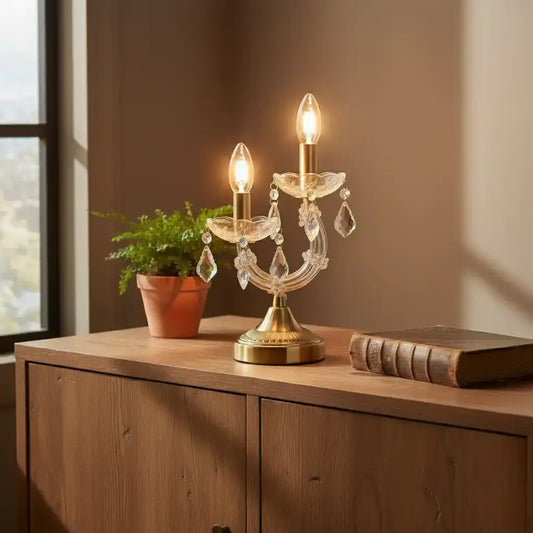 Decorative table lamp with crystal accents on a wooden surface next to a plant and book.