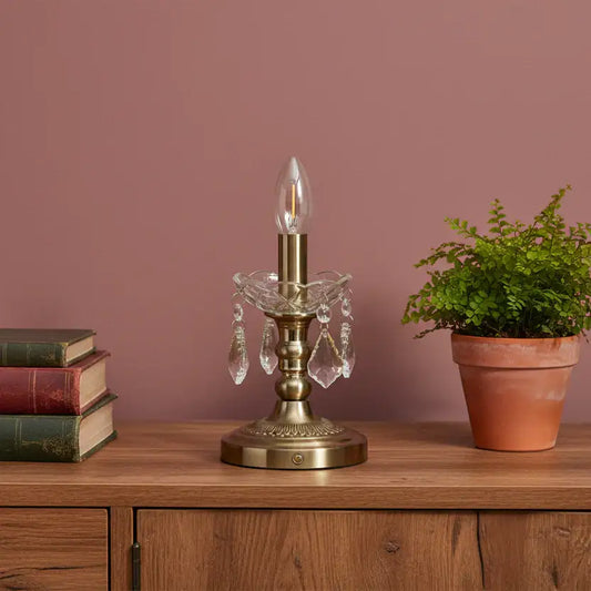 Decorative table lamp with crystal accents on a wooden surface next to books and a plant against a pink wall.