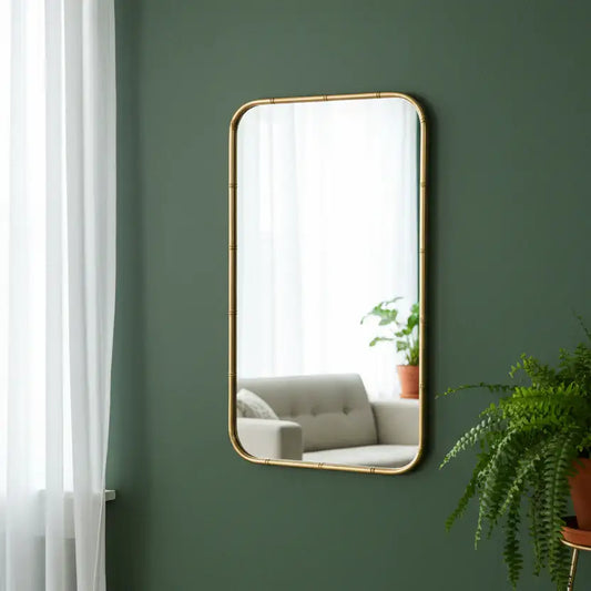 Rectangular mirror with gold frame on a green wall, reflecting a living room with a sofa and plant.