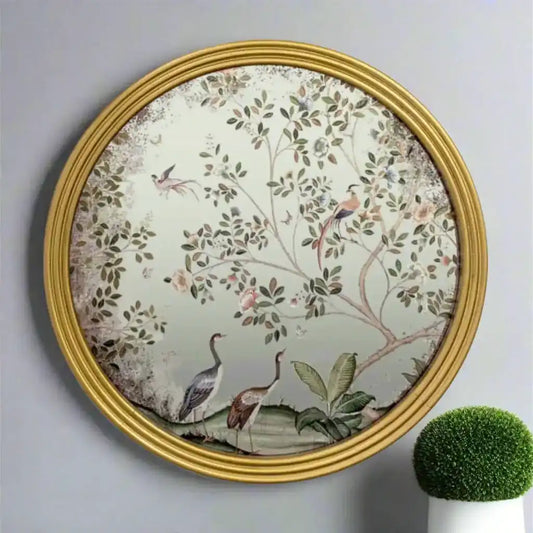 Decorative wall mirror with floral and bird design in a gold frame on a gray wall.