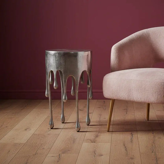 Metallic side table with unique design next to a pink armchair against a red wall.