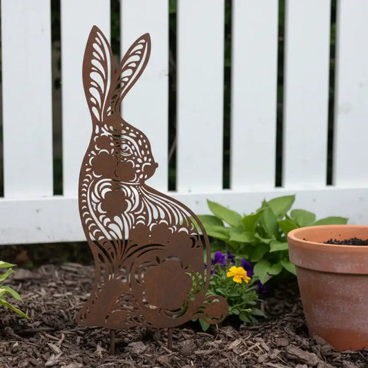 Metal rabbit sculpture in a garden setting with a white fence and potted plant.