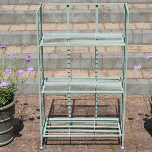 Green metal bakers rack with three shelves on a stone patio.
