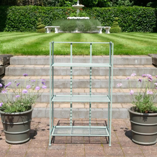 Metal garden shelf with plants on a patio area in front of a fountain.