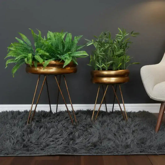 Two potted plants in bronze planters with metal stands on a gray carpet.