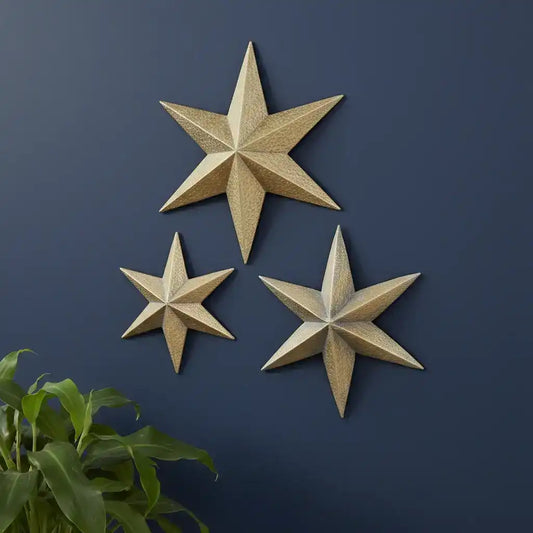 Three gold star-shaped wall decorations on a dark blue wall with a plant at the bottom left corner.