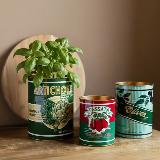 Three repurposed canned food planters with plants on a wooden surface.
