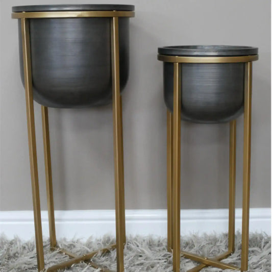 Two black planters on gold stands against a gray wall.