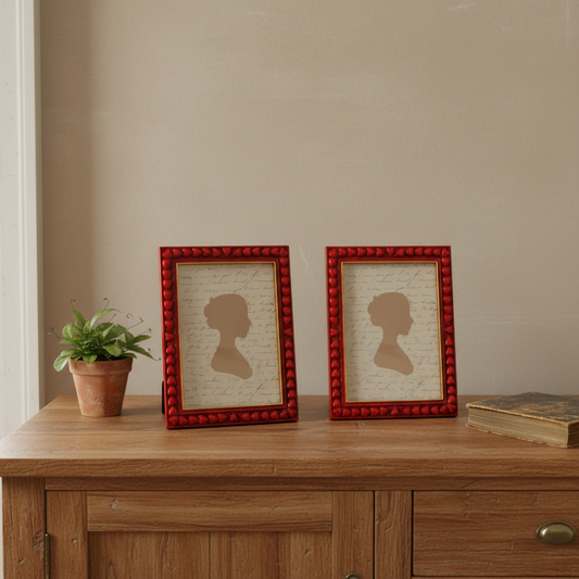 Two red-framed silhouettes on a wooden surface with a plant and book in the background.