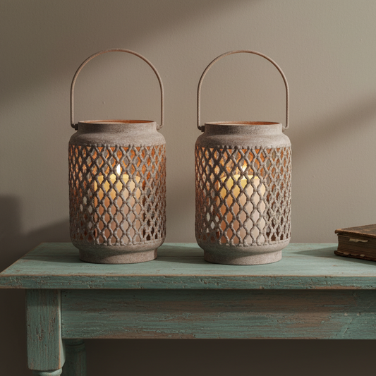 Two rustic metal lantern candles with wire diamond-pattern cutouts and arched handles, placed on a distressed teal table against a warm beige wall.