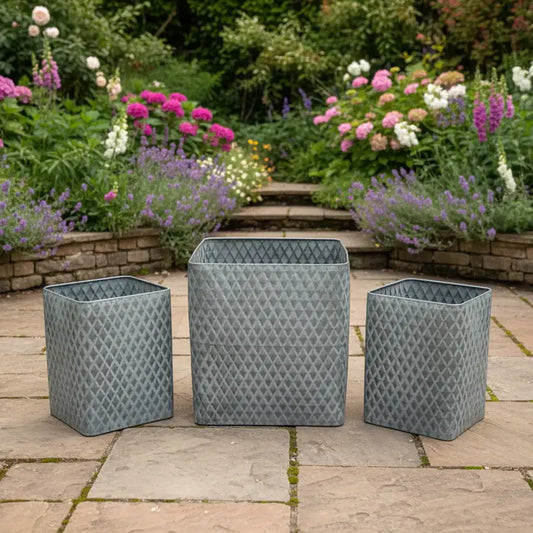 Three gray patterned rectangular planters on a patio with a garden in the background