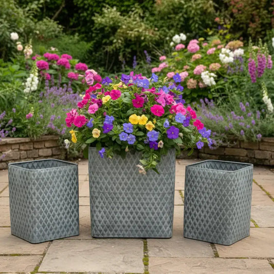 Three decorative metal planters with patterned design containing colorful flowers on a patio.