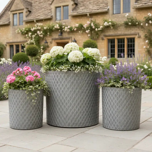 Three decorative planters with flowers in front of a brick building.