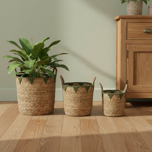 Three woven baskets with plants on a wooden floor next to a wooden cabinet.