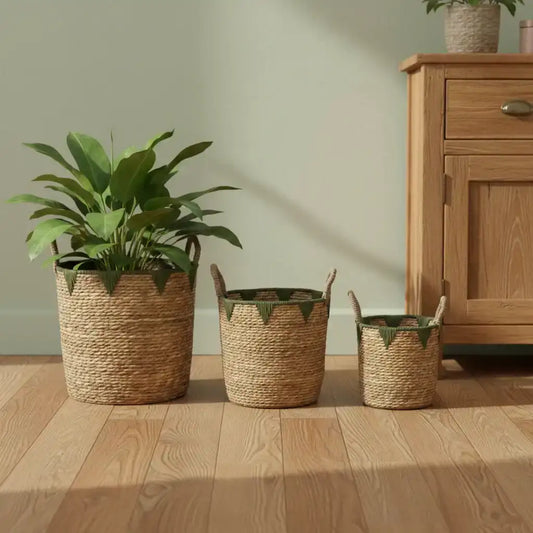 Three woven baskets with plants on a wooden floor next to a wooden cabinet.