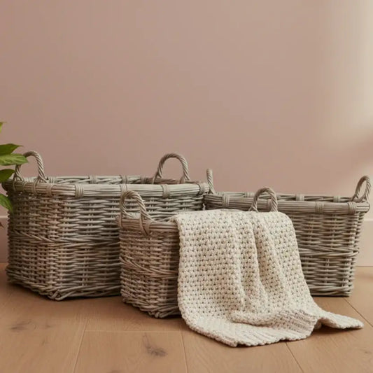 Three woven baskets with a knitted blanket on a wooden floor against a pink wall.