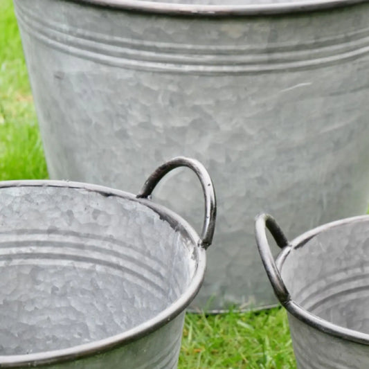Three galvanized metal buckets on a grassy background