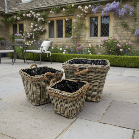 Three wicker planters with black liners on a stone patio in front of a stone building with flowers.