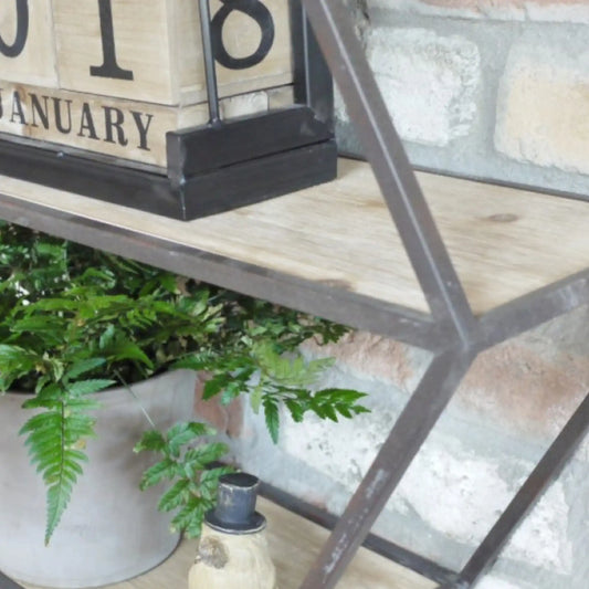 Decorative shelf with plants, a lantern, and a wooden block calendar on a stone wall background.
