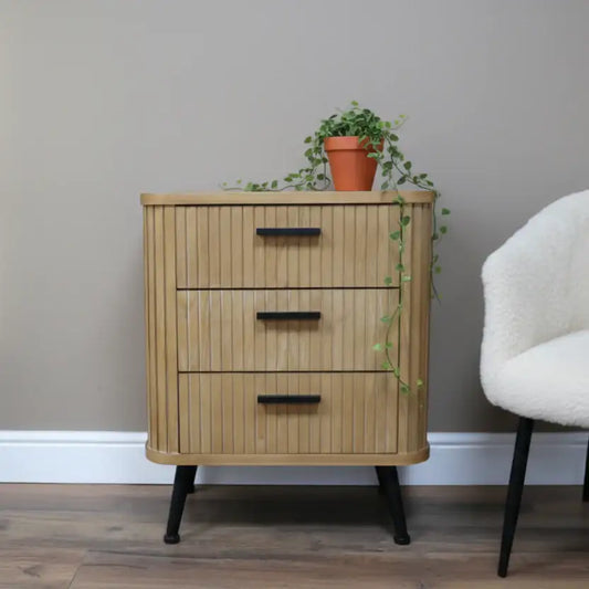 Wooden side table with three drawers, a lamp, and a sculpture on top, next to a plant.