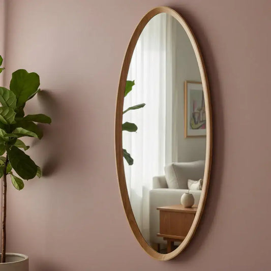 Oval mirror with wooden frame on a pink wall with a plant and part of a room visible in the reflection.