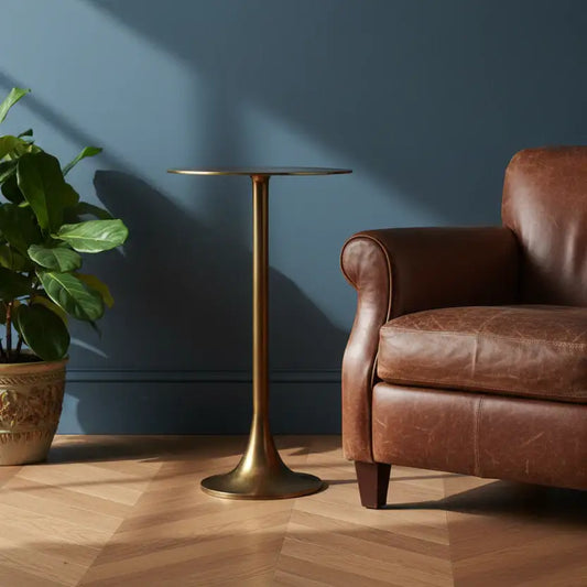 Brown leather armchair and gold side table against a blue wall with a plant on a wooden floor.