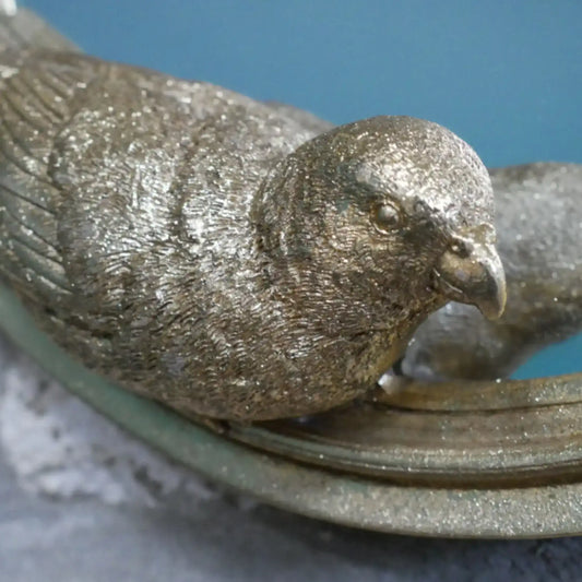Bronze sculpture of a bird perched on a branch with a blue background