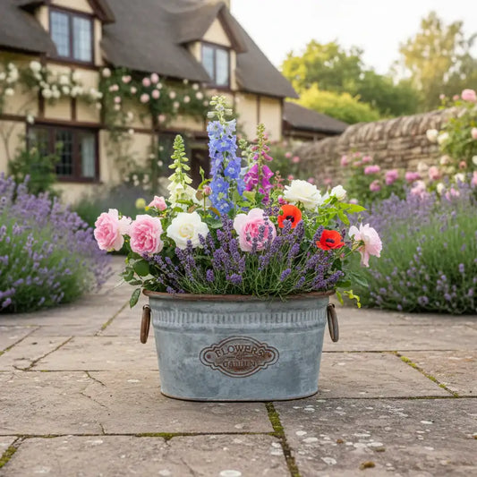 Floral arrangement in a metal bucket on a stone path with a garden and house in the background