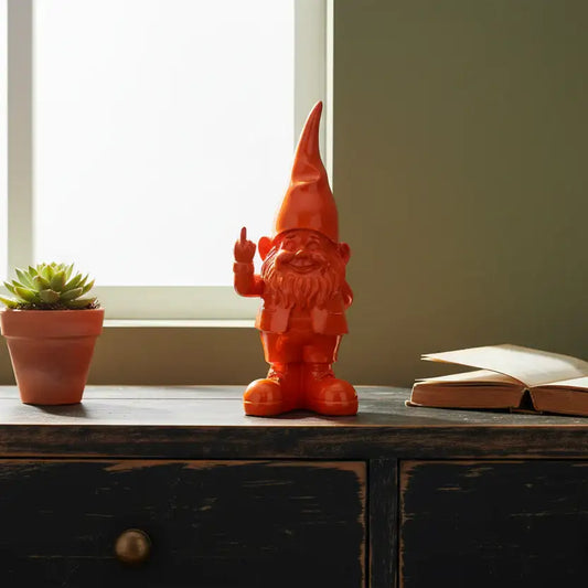 Orange gnome figurine on a wooden surface with a plant and book in the background