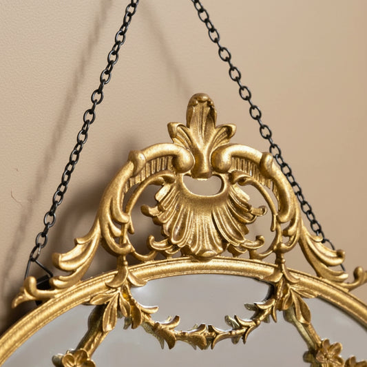 Decorative gold mirror with intricate designs and a chain on a white background